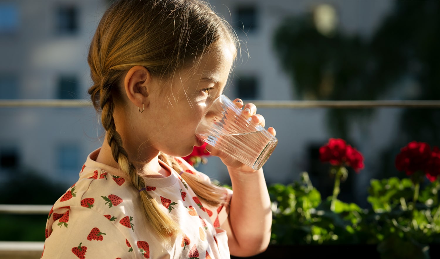 En flicka i sommarklänning dricker vatten ur ett glas.