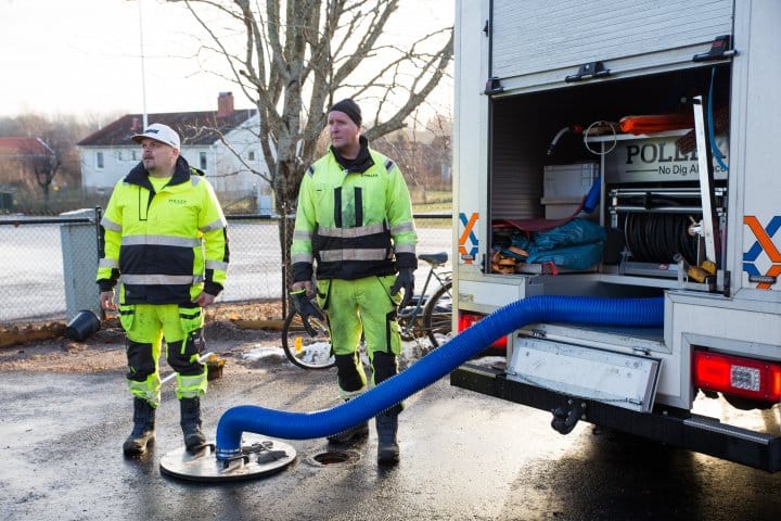 Två arbetare från Pollex står vid ett rör som går ner i en brunn